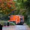 orange trash truck parks on a quiet suburban neighborhood street. Trash cans in the foreground have just been emptied.